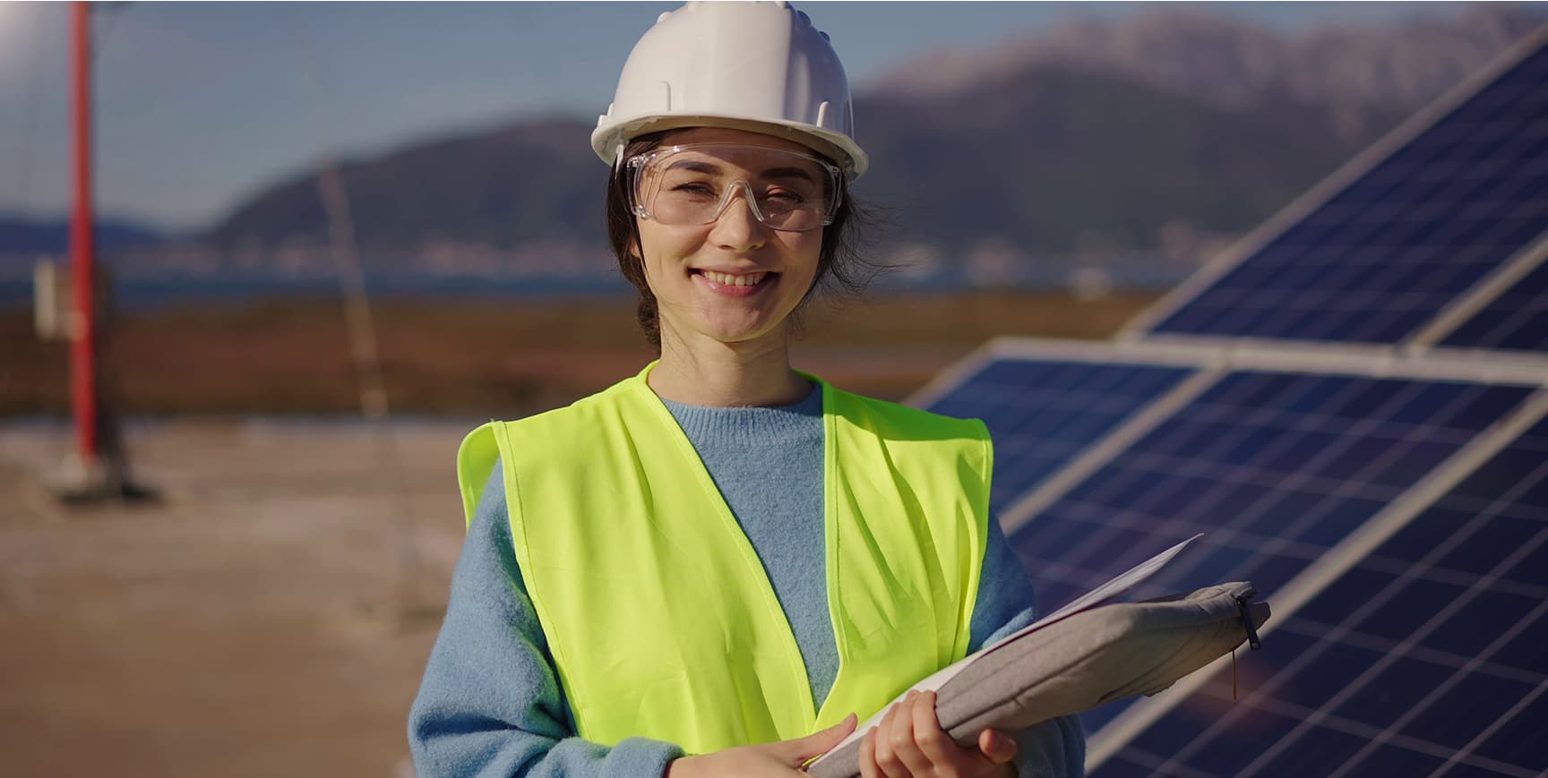 Woman in hi-vis gear smiling and standing in front of solar panels.
